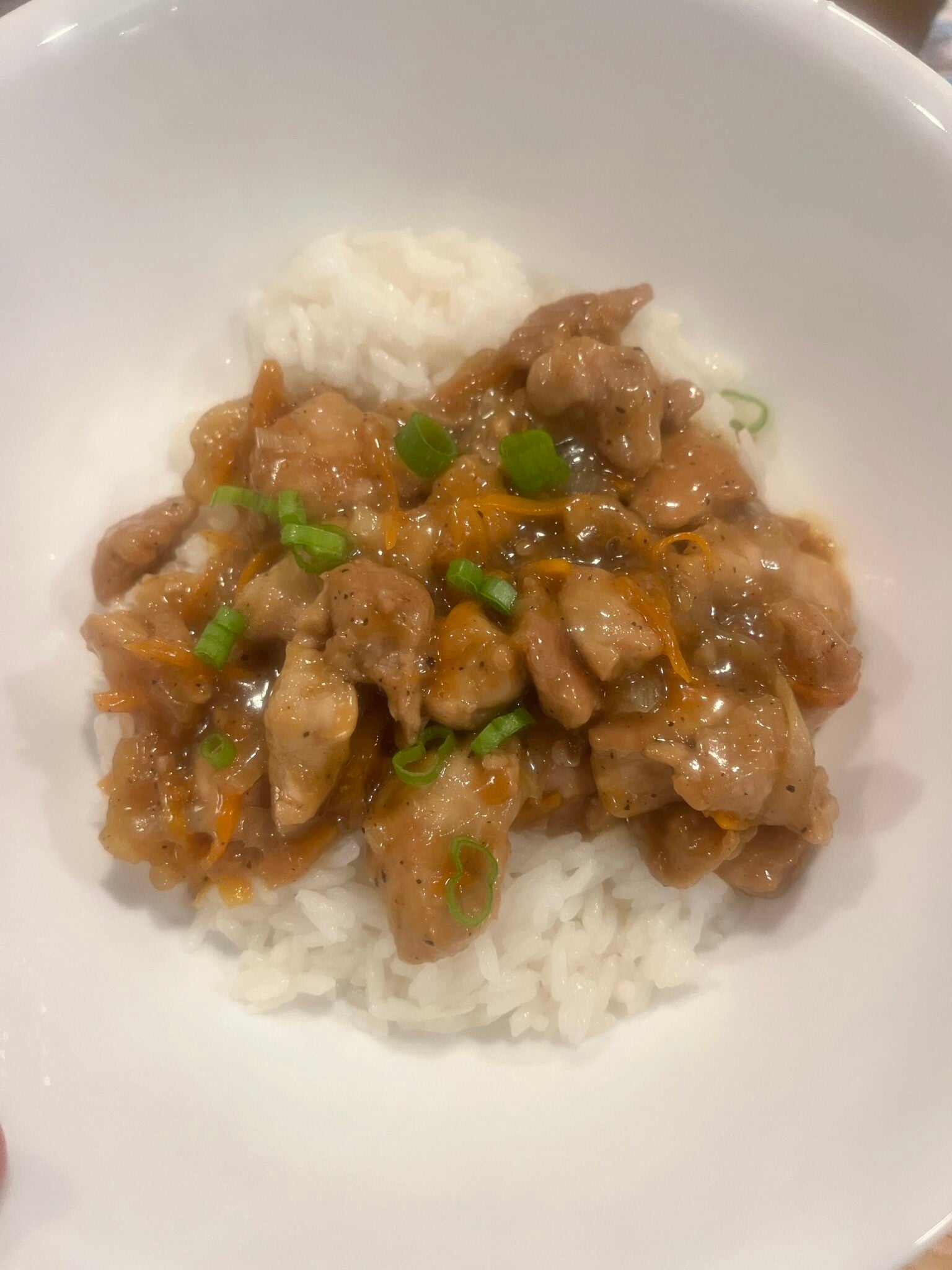 Overhead view of a diced pork dish with carrots and green onions over white rice.